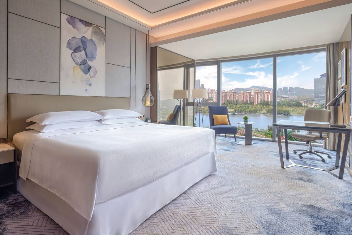 Ein Hotelzimmer mit einem großen Bett, einem Schreibtisch und Blick auf eine Stadtlandschaft und Wasser.