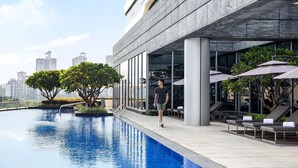 Une piscine moderne, située dans un espace aménagé avec des chaises longues, offrant une vue dégagée sur les gratte-ciel de la ville et dont l’entretien est impeccable.