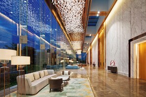 A modern lobby with a glass wall, a sofa, chairs, and a patterned rug.