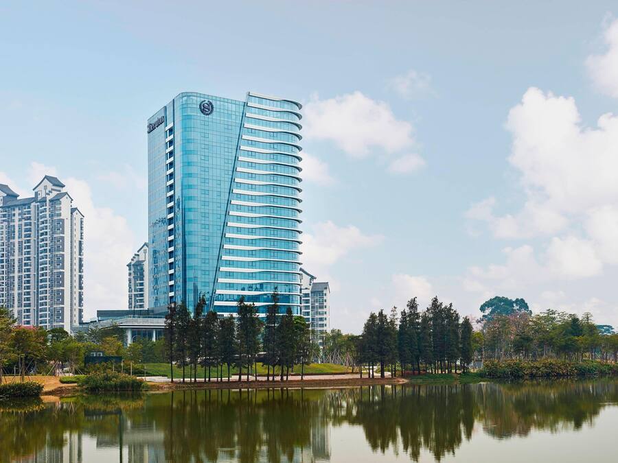 Een modern hotel met een gebogen glazen gevel, gelegen aan een rustig meer met een weerspiegeling van het gebouw.