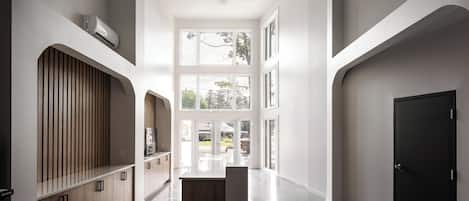 A spacious hallway with a wooden cabinet, a black door, and a large window providing natural light.