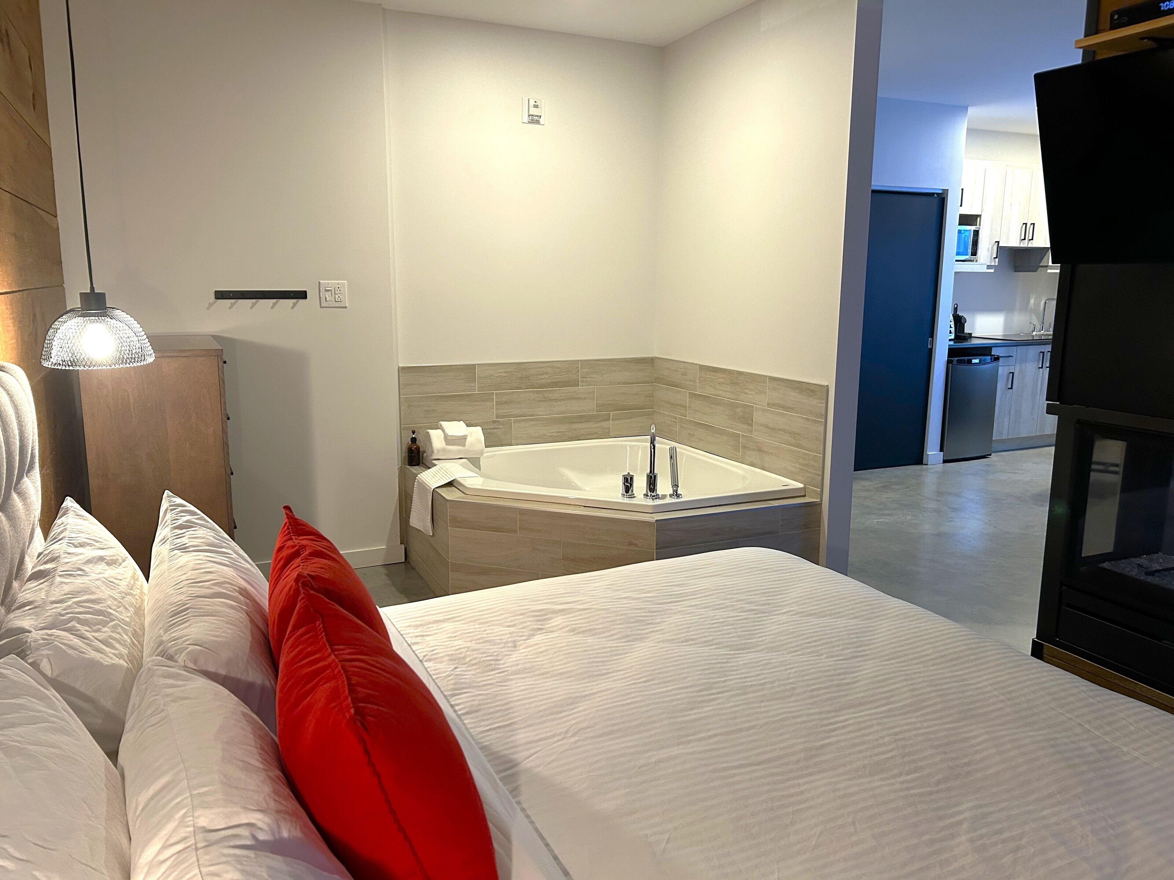 Un dormitorio moderno con una cama grande, una bañera empotrada y una zona de cocina visible.