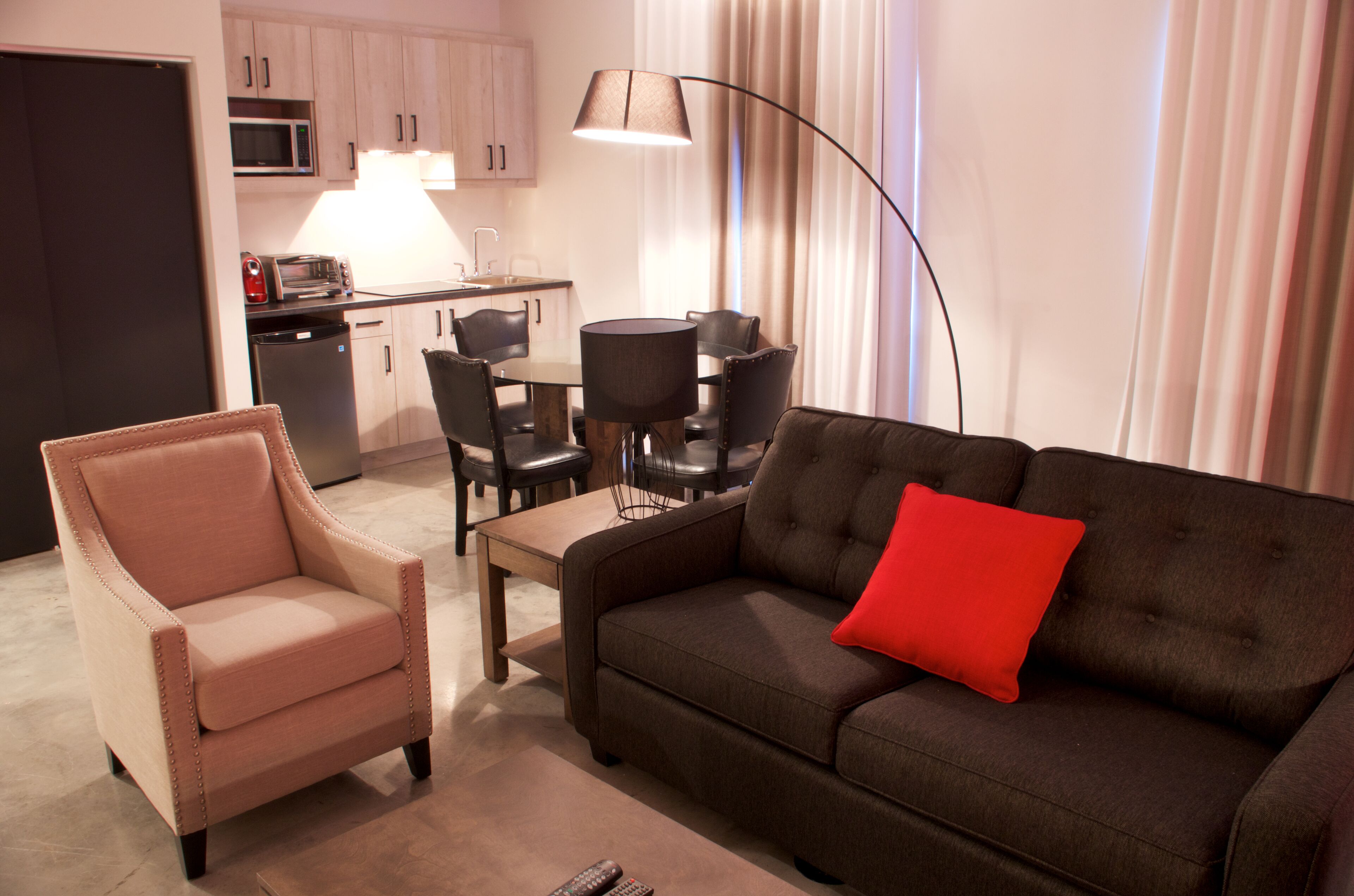 A compact living space with a sofa, armchair, dining table, and chairs. A microwave and dishwasher are visible in the background.