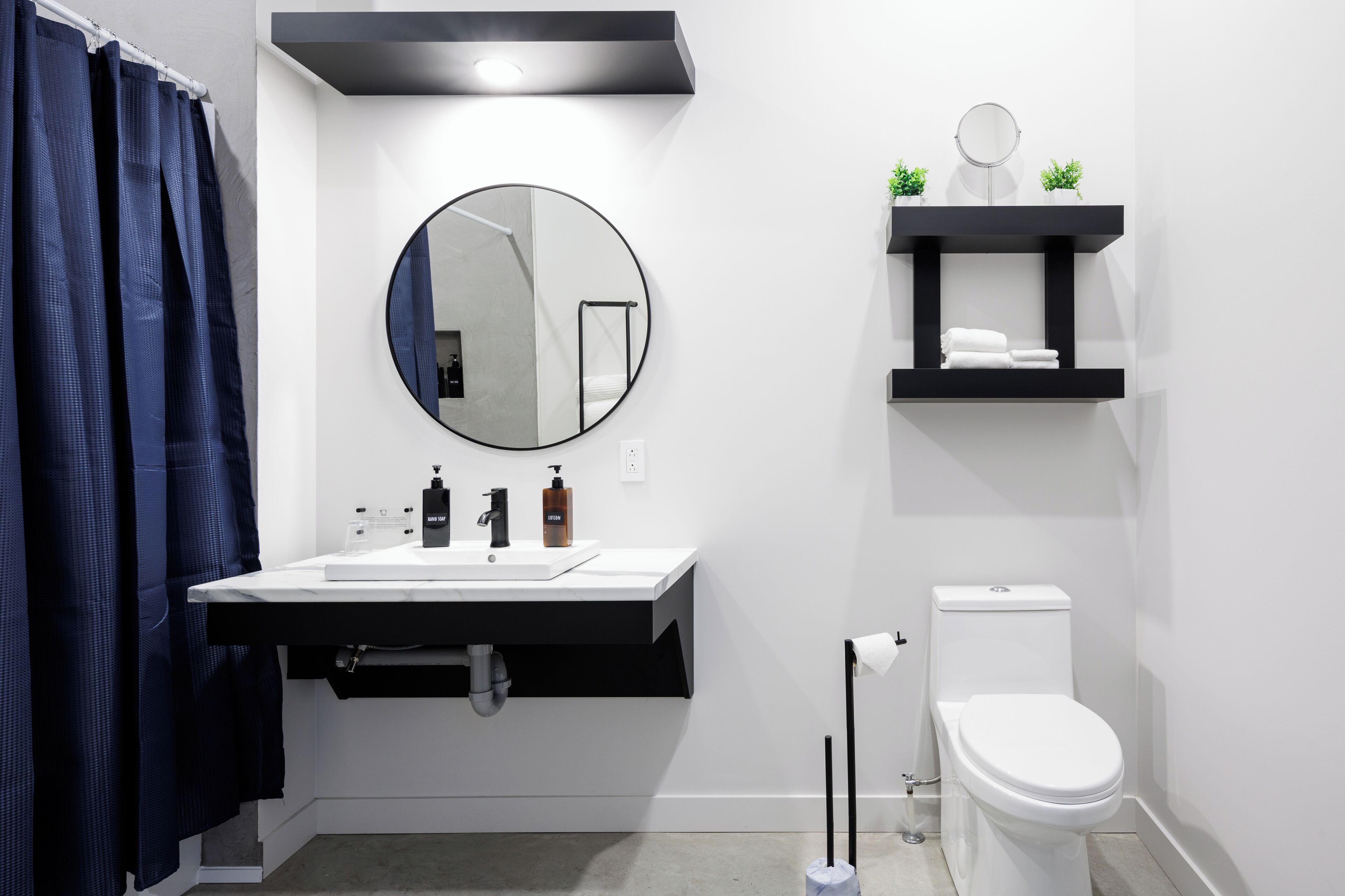 A modern bathroom with a white sink, black countertop, round mirror, and white toilet.