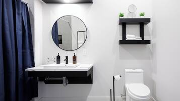 A modern bathroom with a white sink, black countertop, round mirror, and white toilet.