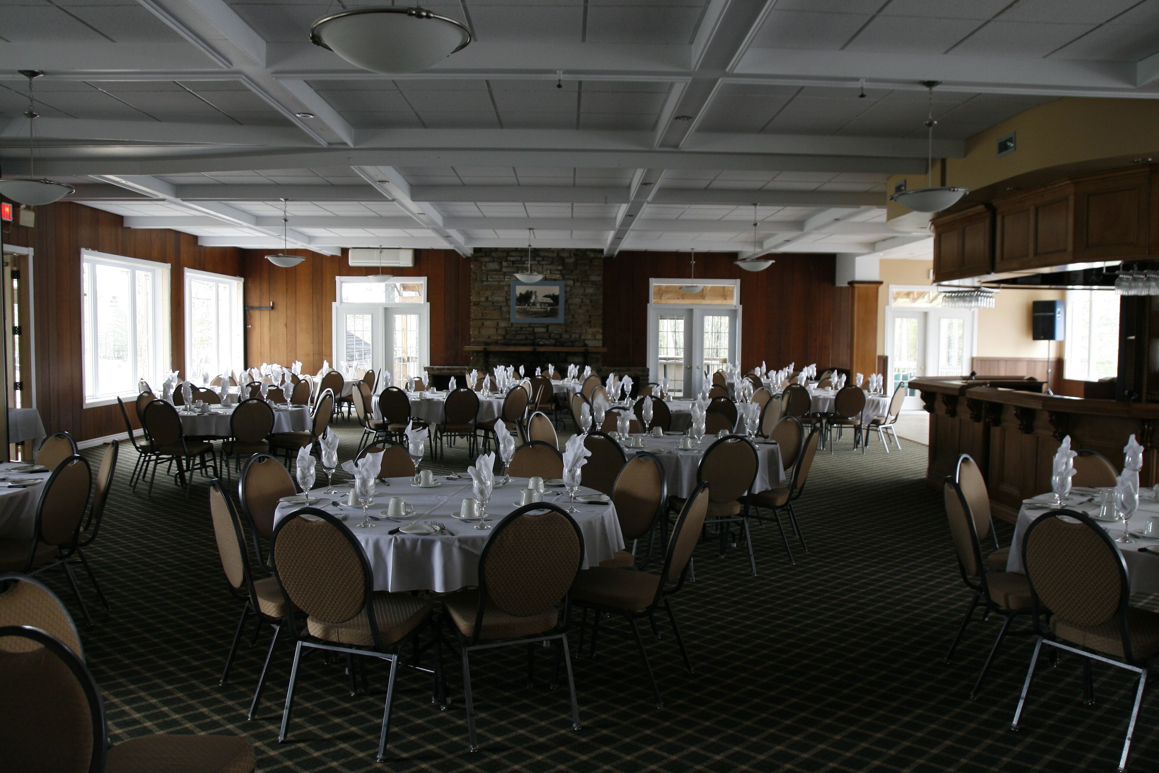 Un amplio salón de banquetes con varias mesas redondas dispuestas para comidas, con manteles y sillas blancos.