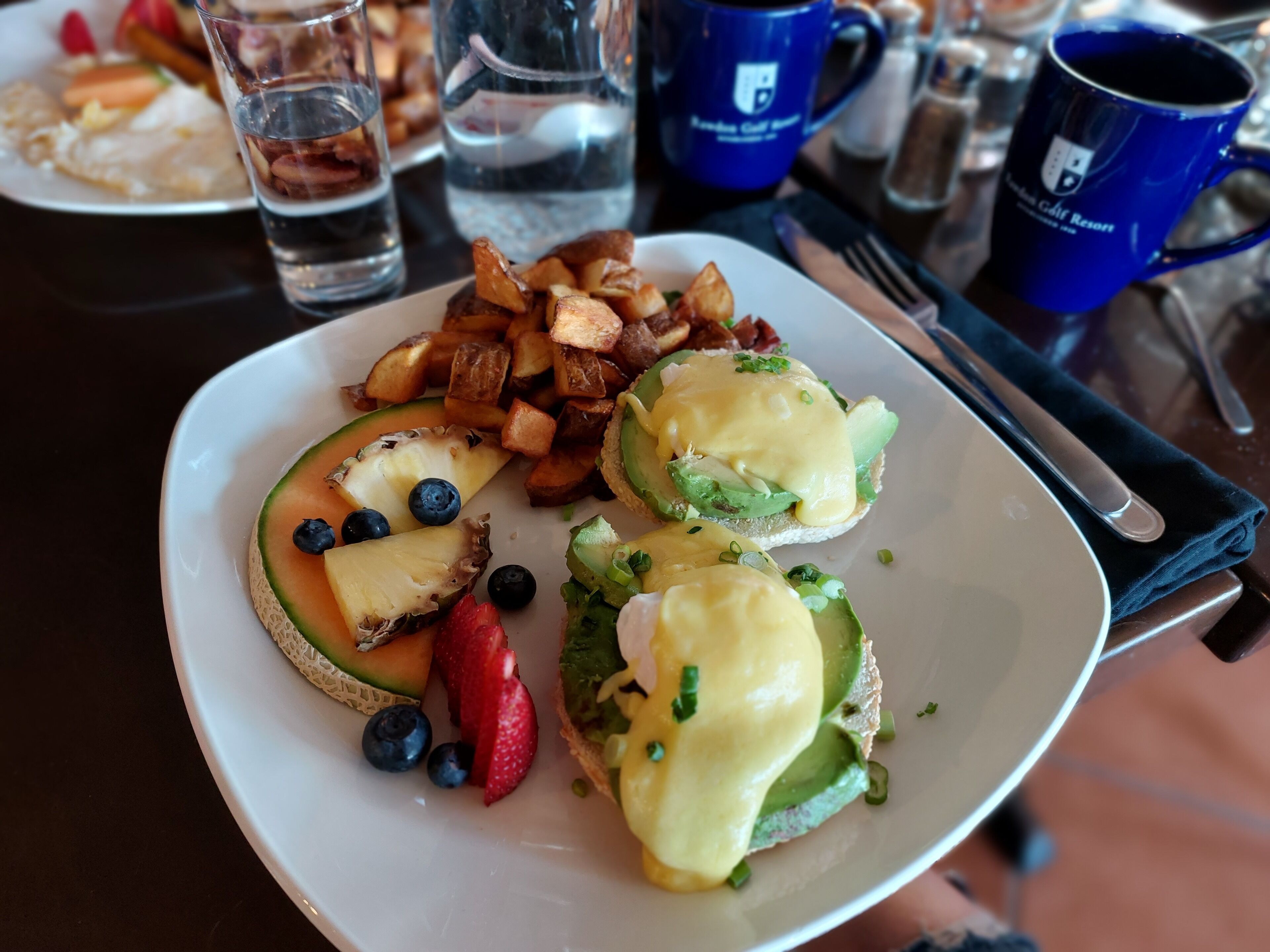 Een ontbijtje met eggs benedict, fruit en aardappelen.