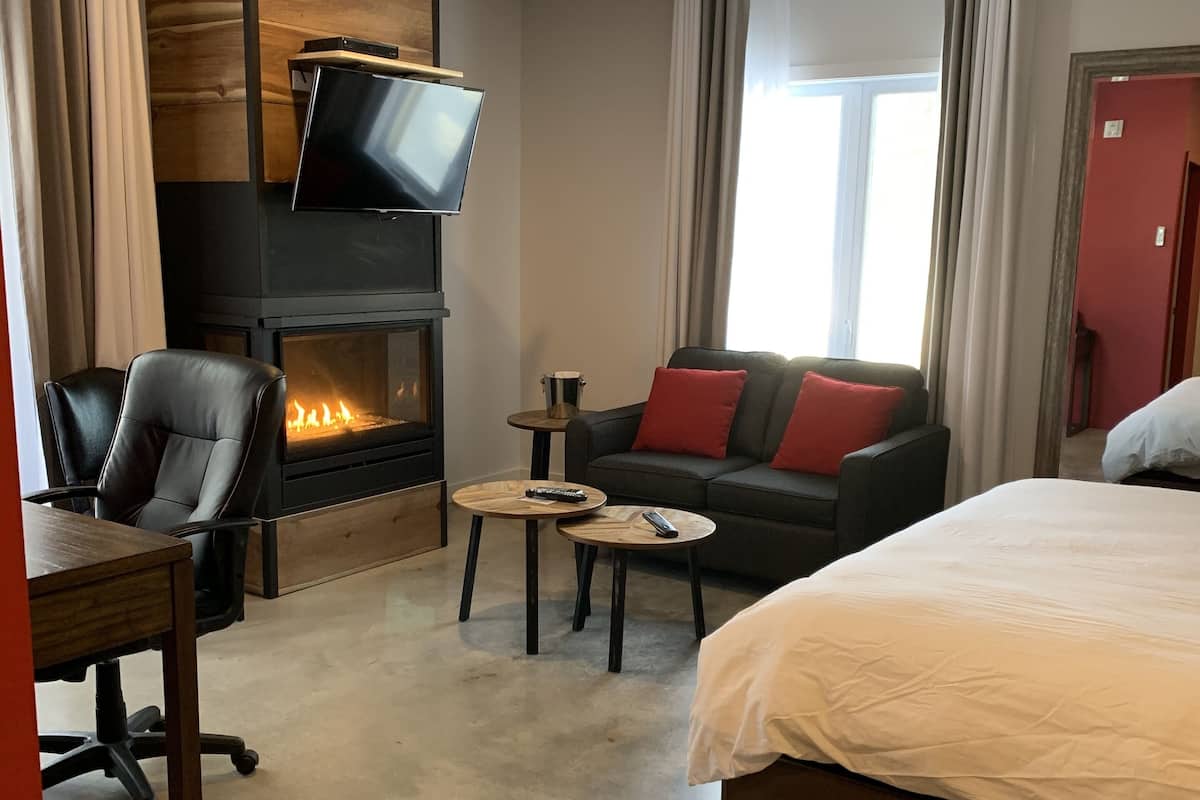 Una habitación de hotel moderna con chimenea, televisor de pantalla plana, sofá con cojines rojos, cama y escritorio con silla.