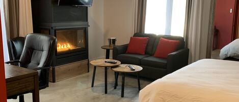 Ein modernes Hotelzimmer mit Kamin, einem Flachbildfernseher, einer Couch mit roten Kissen, einem Bett und einem Schreibtisch mit Stuhl.