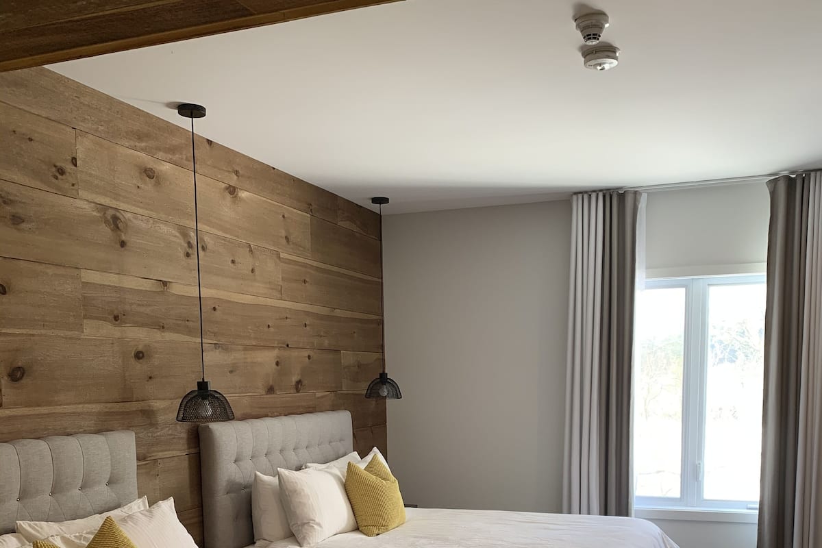 Un dormitorio moderno con dos camas, paneles de madera en la pared y un ventanal con cortinas.