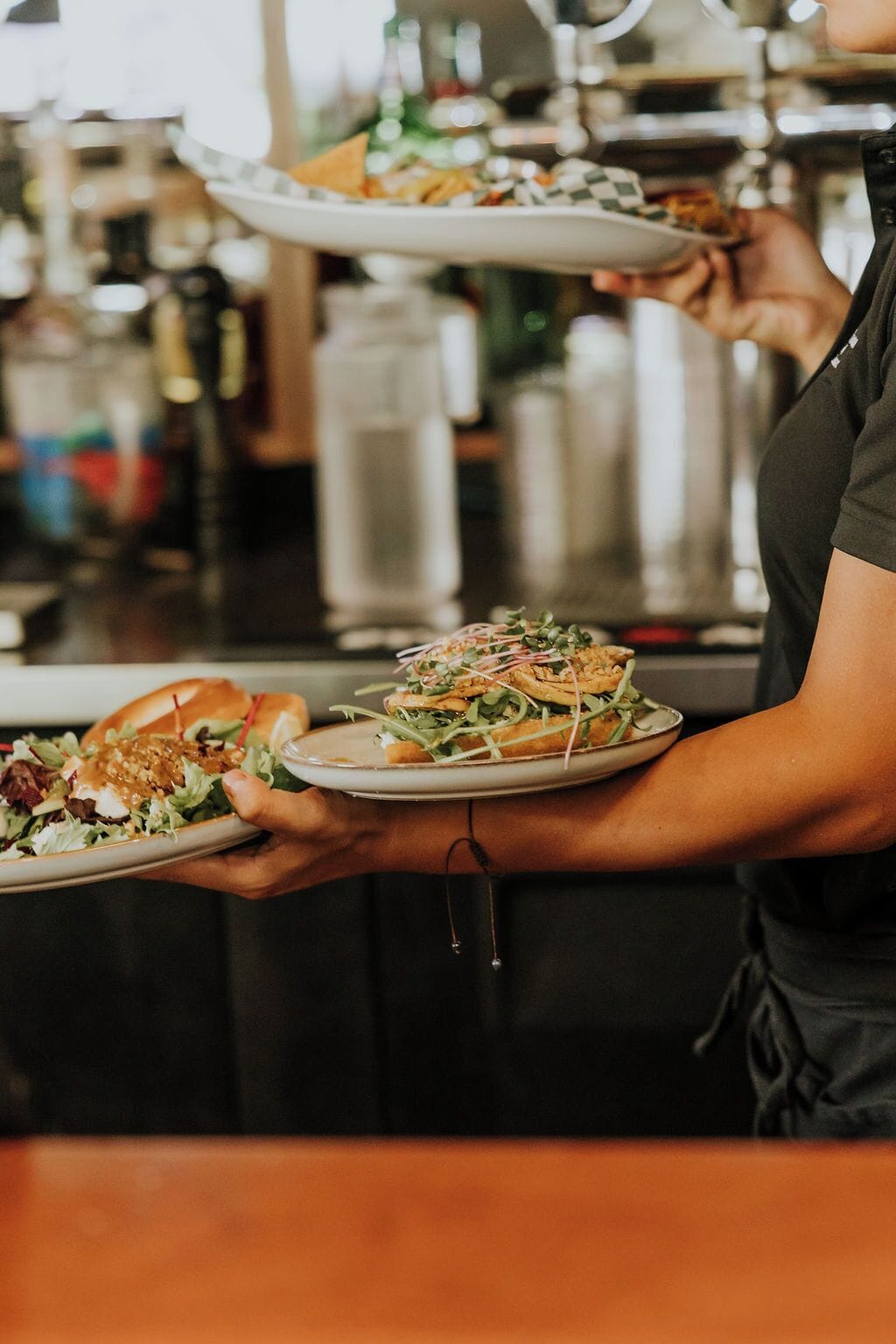 A person holding two plates, one with a burger and the other with a salad.