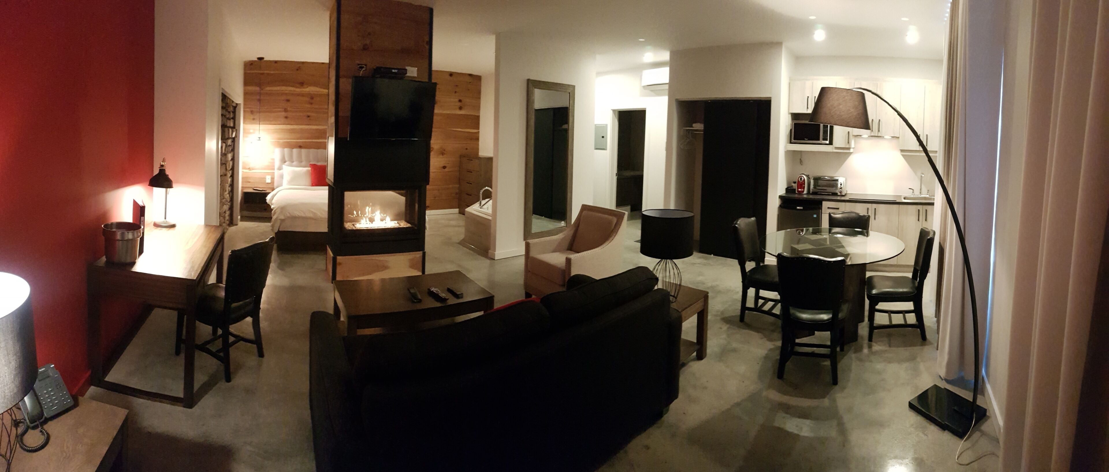 A modern hotel room with a fireplace, a dining area, and a kitchen.