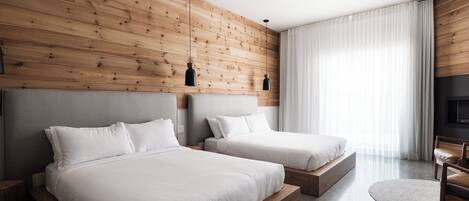 A modern hotel room with two beds, wooden panel walls, a large window with curtains, and a flat-screen TV.
