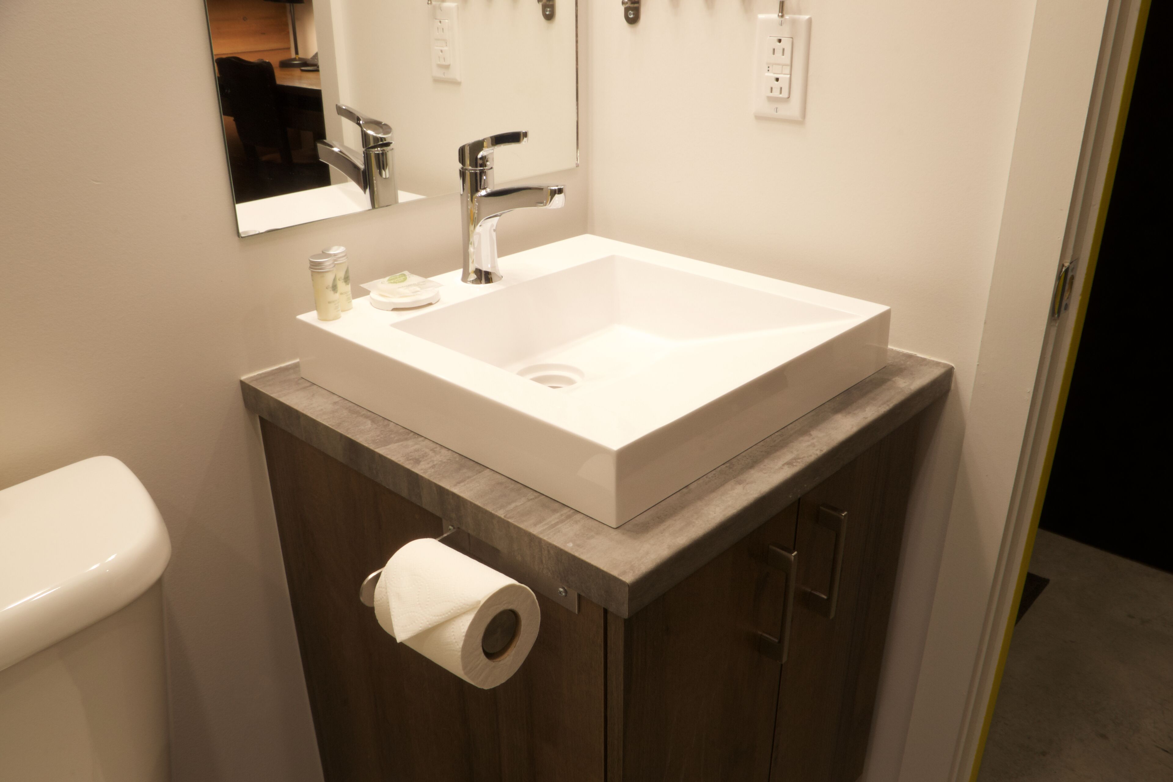 Een badkamer met een witte wastafel, een spiegel, een toilet en een rol toiletpapier.