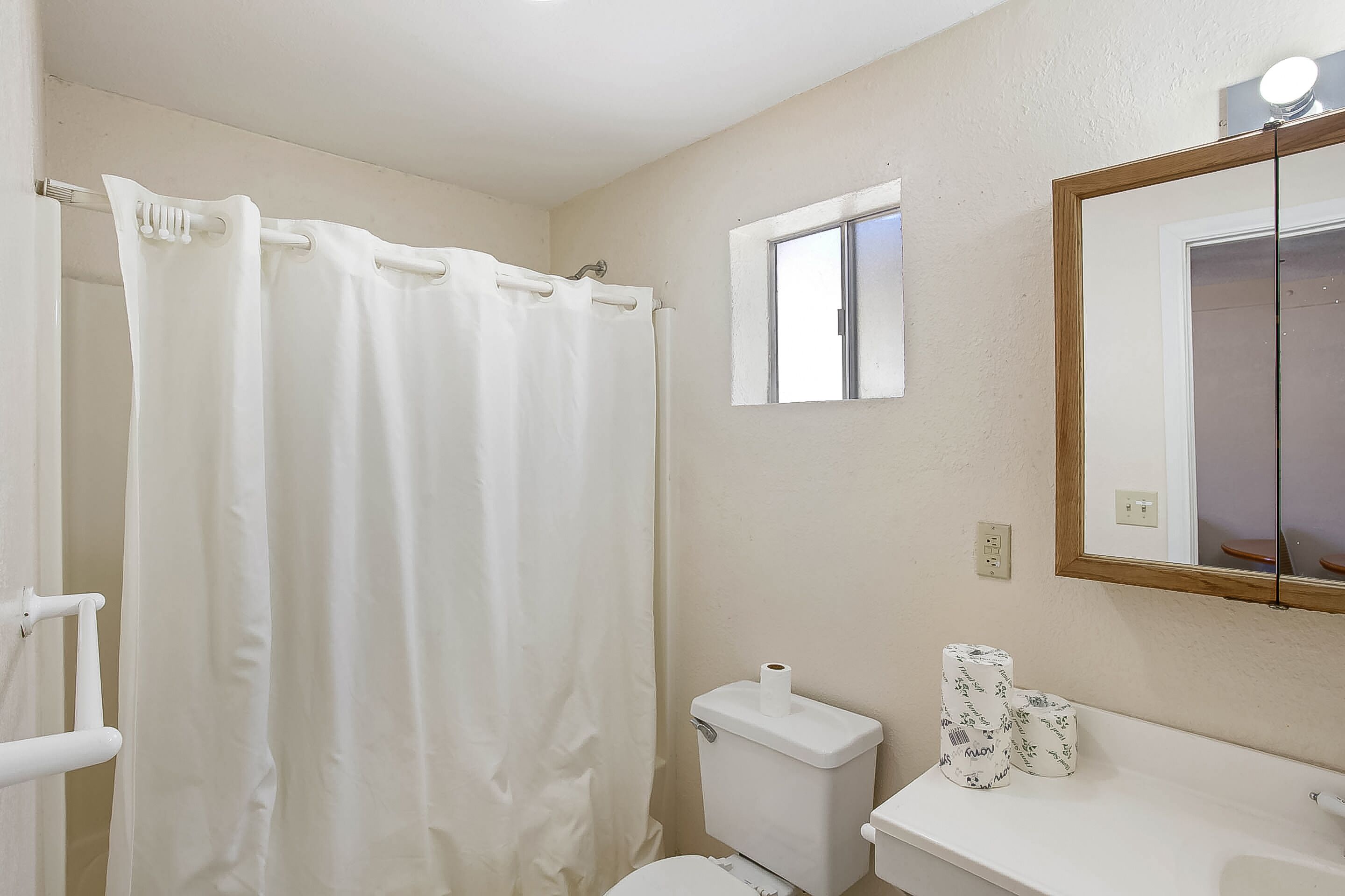 Een badkamer met een witte douchegordijn, een toilet, een wastafel met twee rollen toiletpapier, en een spiegel boven de wastafel.
