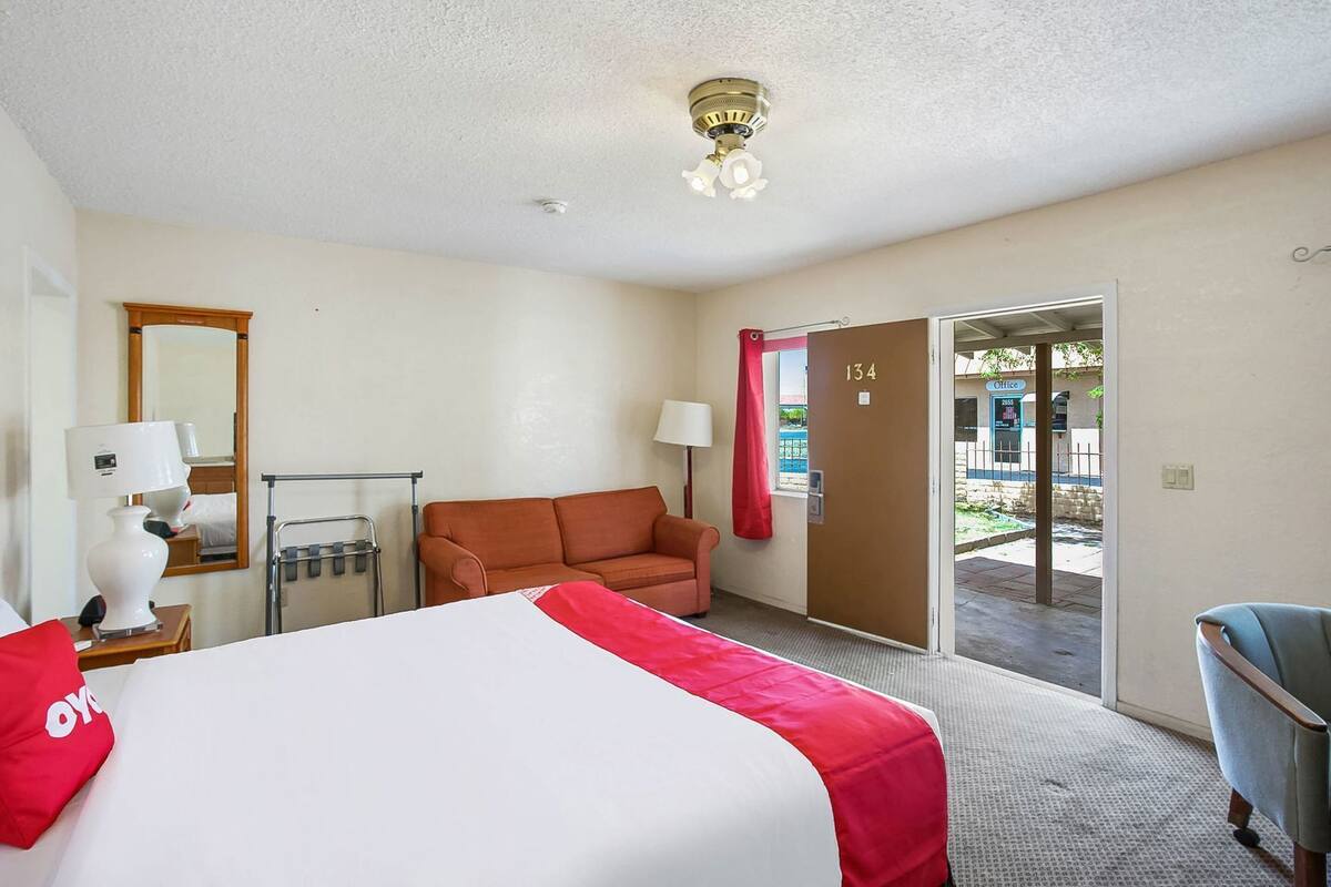 Une chambre d’hôtel comprenant un lit, un canapé, un bureau avec une lampe, une chaise et une porte donnant sur un espace extérieur.