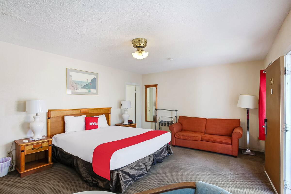 Une chambre d’hôtel avec un lit, un canapé rouge, une table de chevet en bois, une lampe et un miroir.