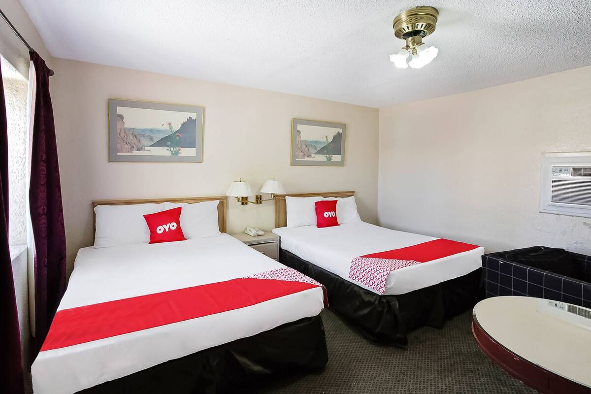 Une chambre d’hôtel avec deux lits, chacun recouvert d’une couvre-lit rouge et blanche, une table de chevet avec une lampe et un climatiseur fixé au mur.