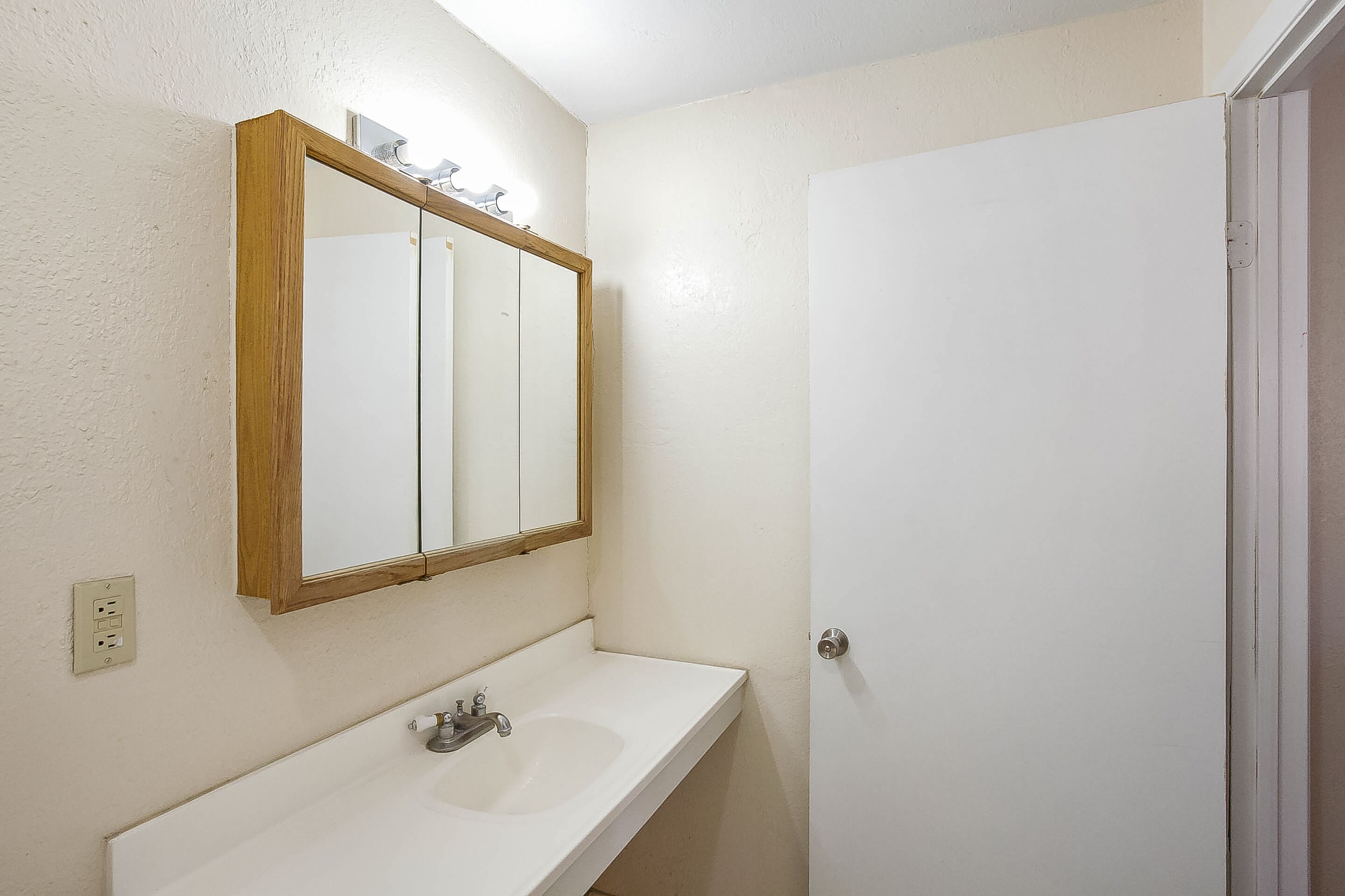 Une salle de bain avec un lavabo blanc, un miroir encadré en bois et une porte blanche.