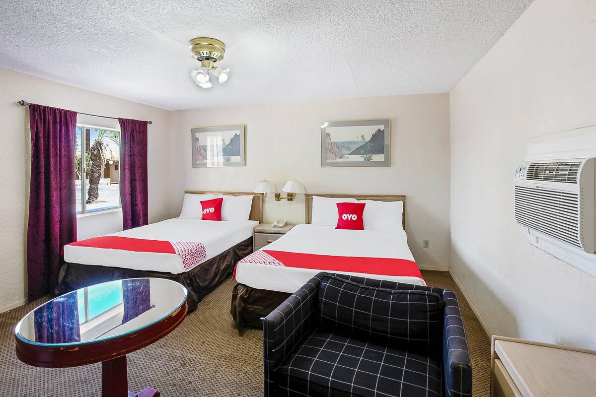 Une chambre d’hôtel avec deux lits, une petite table, une chaise et un appareil de climatisation.
