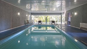 An indoor swimming pool with a clear view of the outdoors, a ceiling with recessed lighting, and a seating area with chairs and tables. - Hotel Galo Vermelho (Gramado)