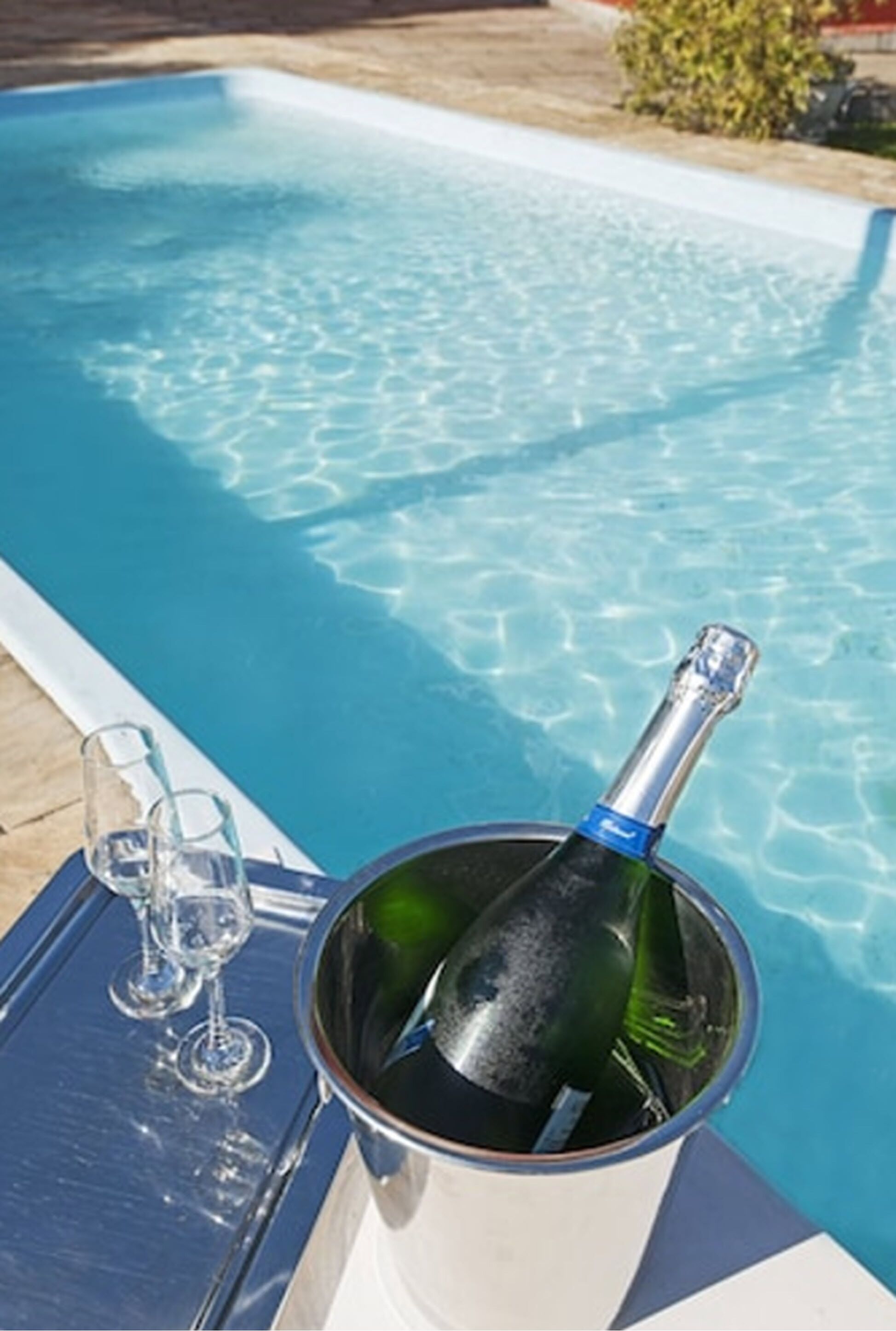 A poolside setting with a bottle of champagne and two glasses on a tray.