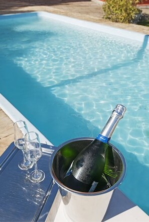 Escena junto a la piscina con una botella de champán y dos copas sobre una bandeja.