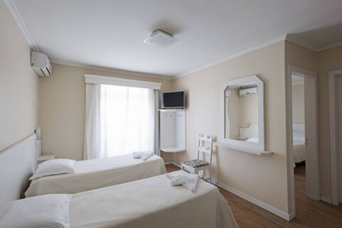 Ein Hotelzimmer mit zwei Betten, einem Fernseher, einem Spiegel und einem Fenster mit Vorhängen.