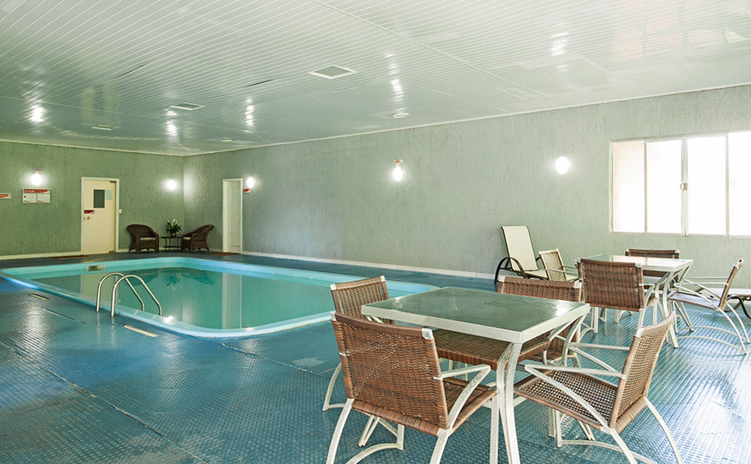 A swimming pool area with lounge chairs and tables, a door, and a window.