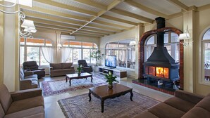 A spacious living room with a fireplace, comfortable seating, and large windows. - Hotel Galo Vermelho (Gramado)