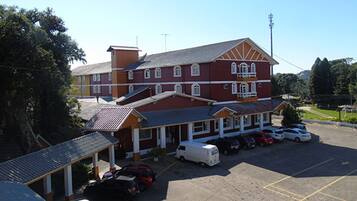 A large, multi-story building with a red facade and white trim, featuring a covered parking area with several cars and a white van.