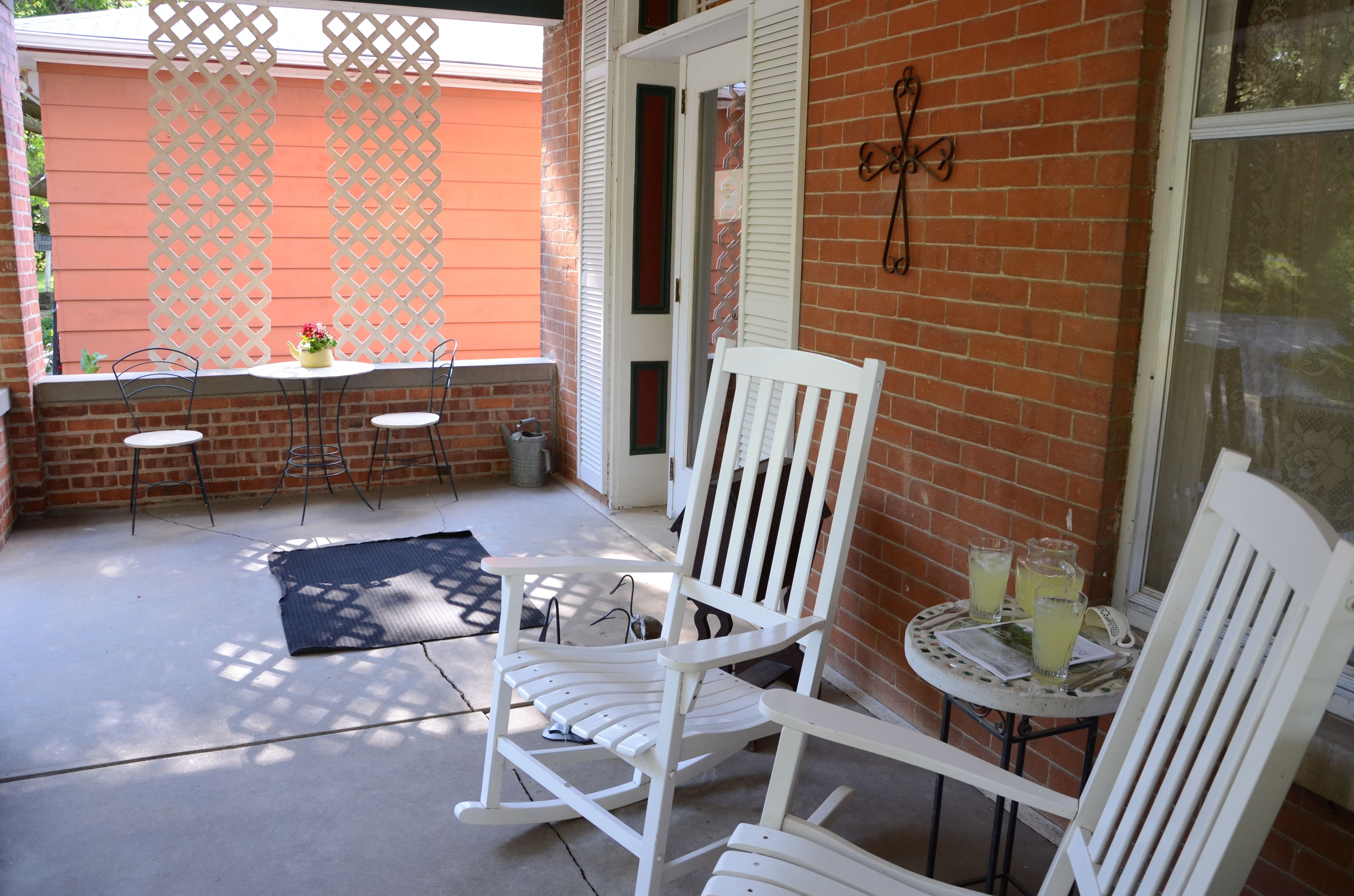 A patio area with a white rocking chair, a small round table with drinks, and a lattice screen.