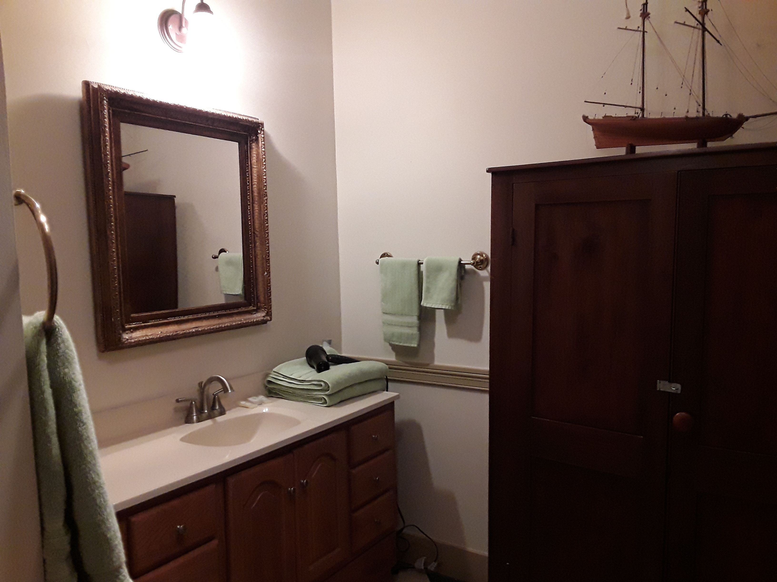 A bathroom with a wooden vanity, a mirror, and a ship model on top of a cabinet.