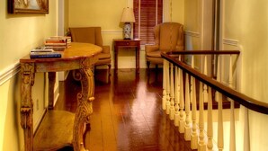 A hallway with a wooden staircase, a chandelier, a dining area with a table and chairs, and a painting on the wall. - Emma's Bed and Breakfast (Springfield)