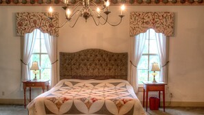 A bedroom with a large bed, two bedside tables, a chandelier, and floral-patterned curtains. - Emma's Bed and Breakfast (Springfield)