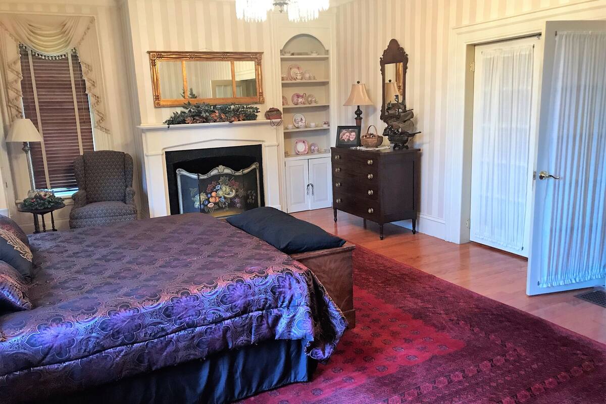 Un dormitorio con una cama grande, una chimenea, un tocador y una puerta.