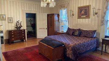 A bedroom with a large bed, a wooden dresser, a chandelier, and a door labeled "Sydney's Suite".