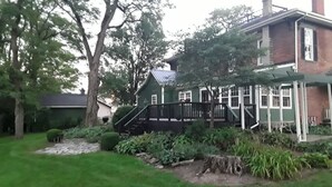 A green house with a wooden deck, surrounded by a garden with various plants and a small pond. - Emma's Bed and Breakfast (Springfield)