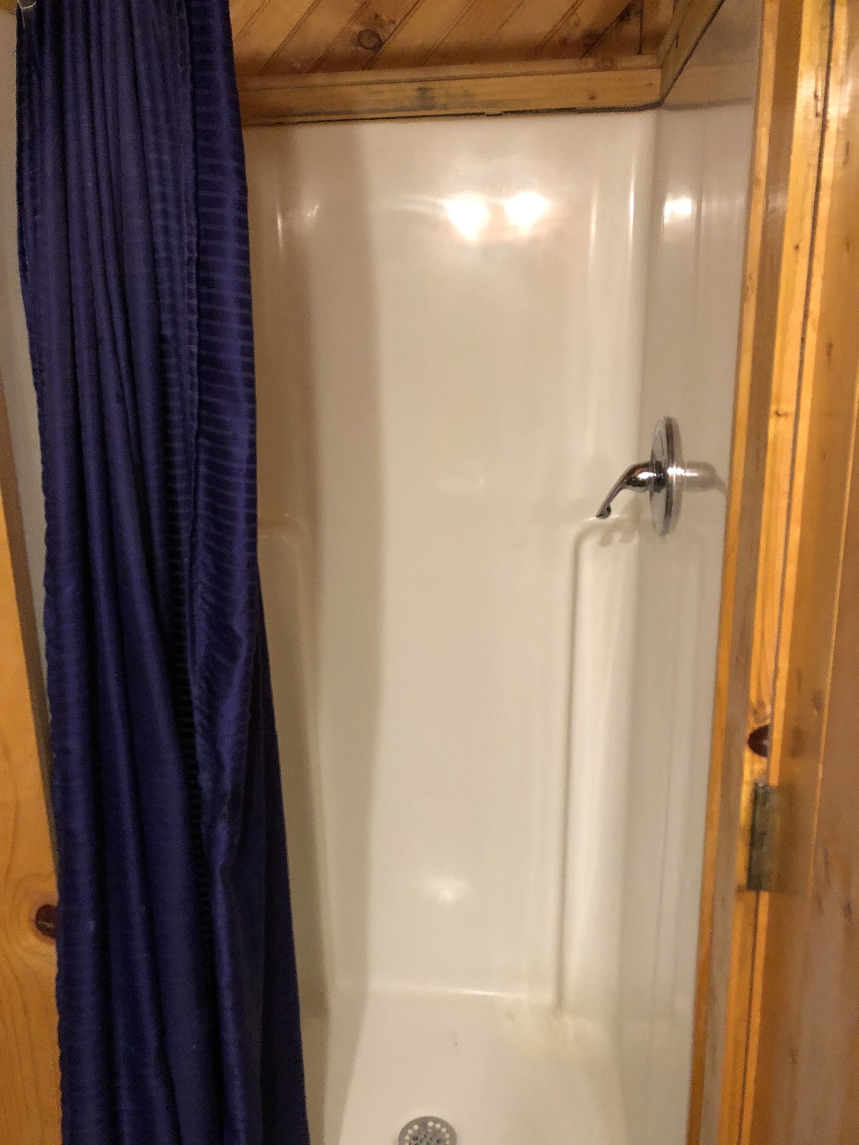 A shower with a wooden ceiling and a white wall.