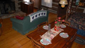 Ein gemütliches Wohnzimmer mit einem Holzesstisch, gedeckt für zwei Personen, einem grünen Sofa und einem Kamin.