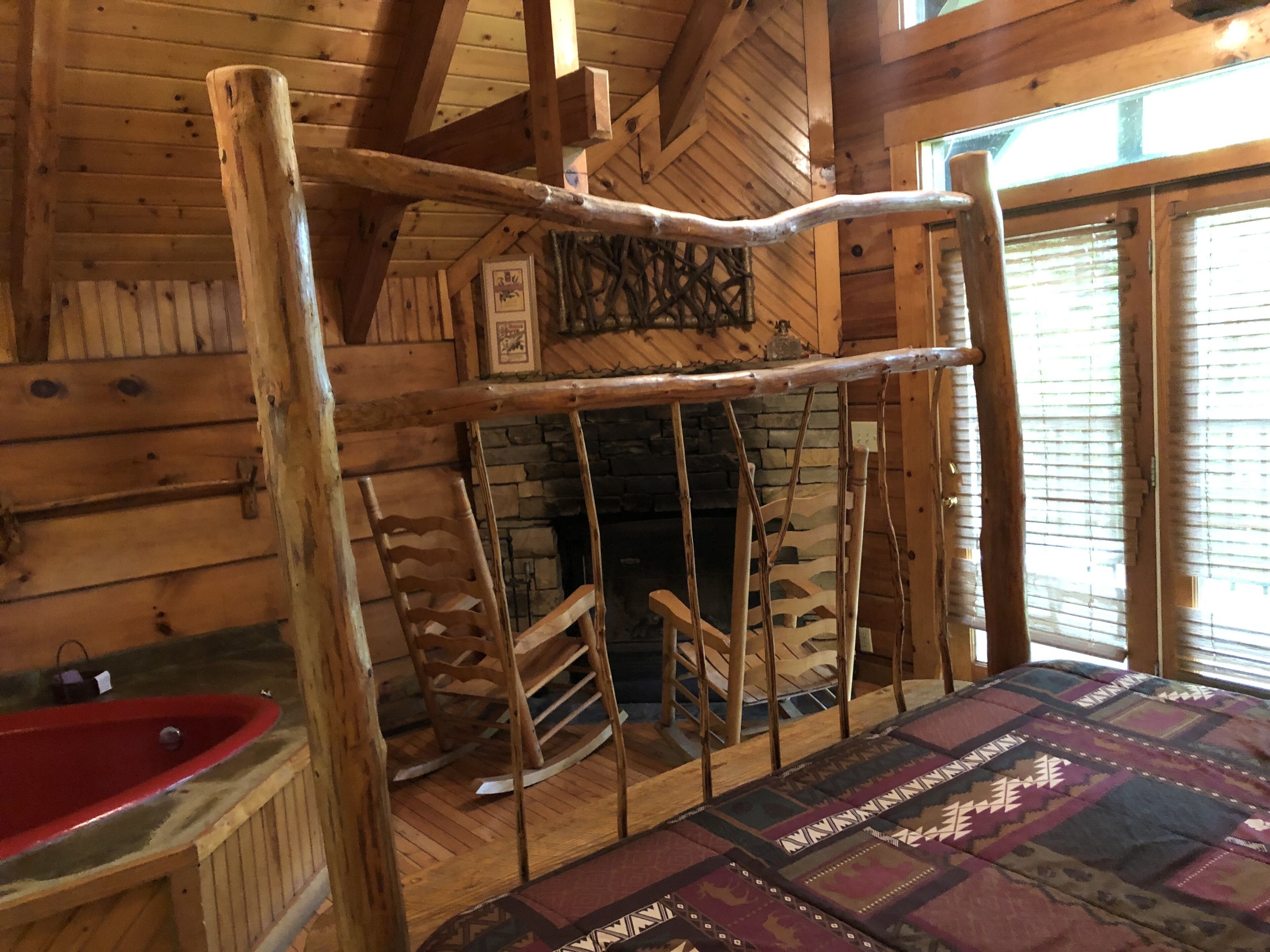 A rustic wooden interior with a stone fireplace, wooden rocking chairs, and a red sink.