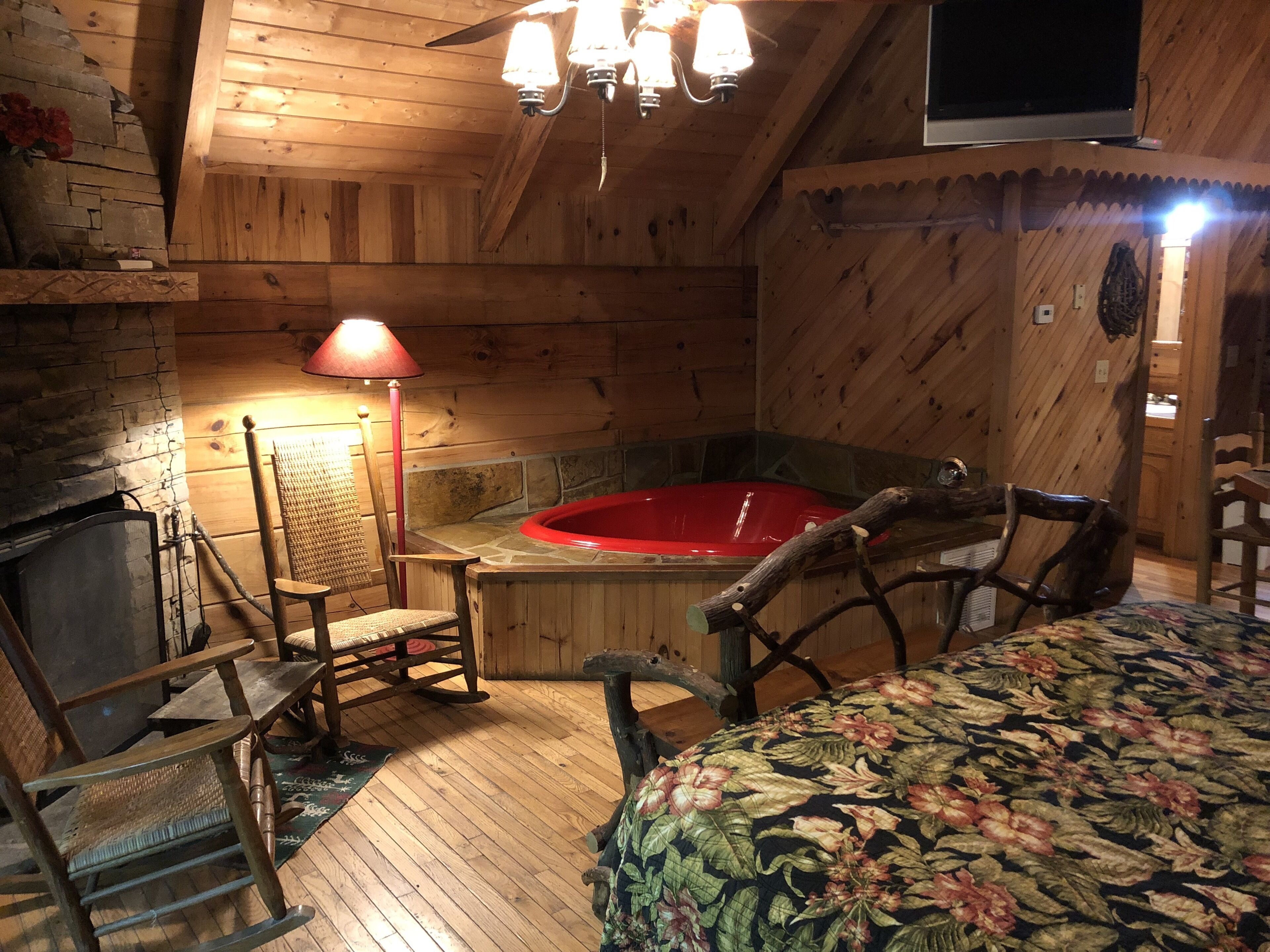A cozy cabin interior with a wooden interior, a stone fireplace, a red hot tub, and a television mounted on the wall.