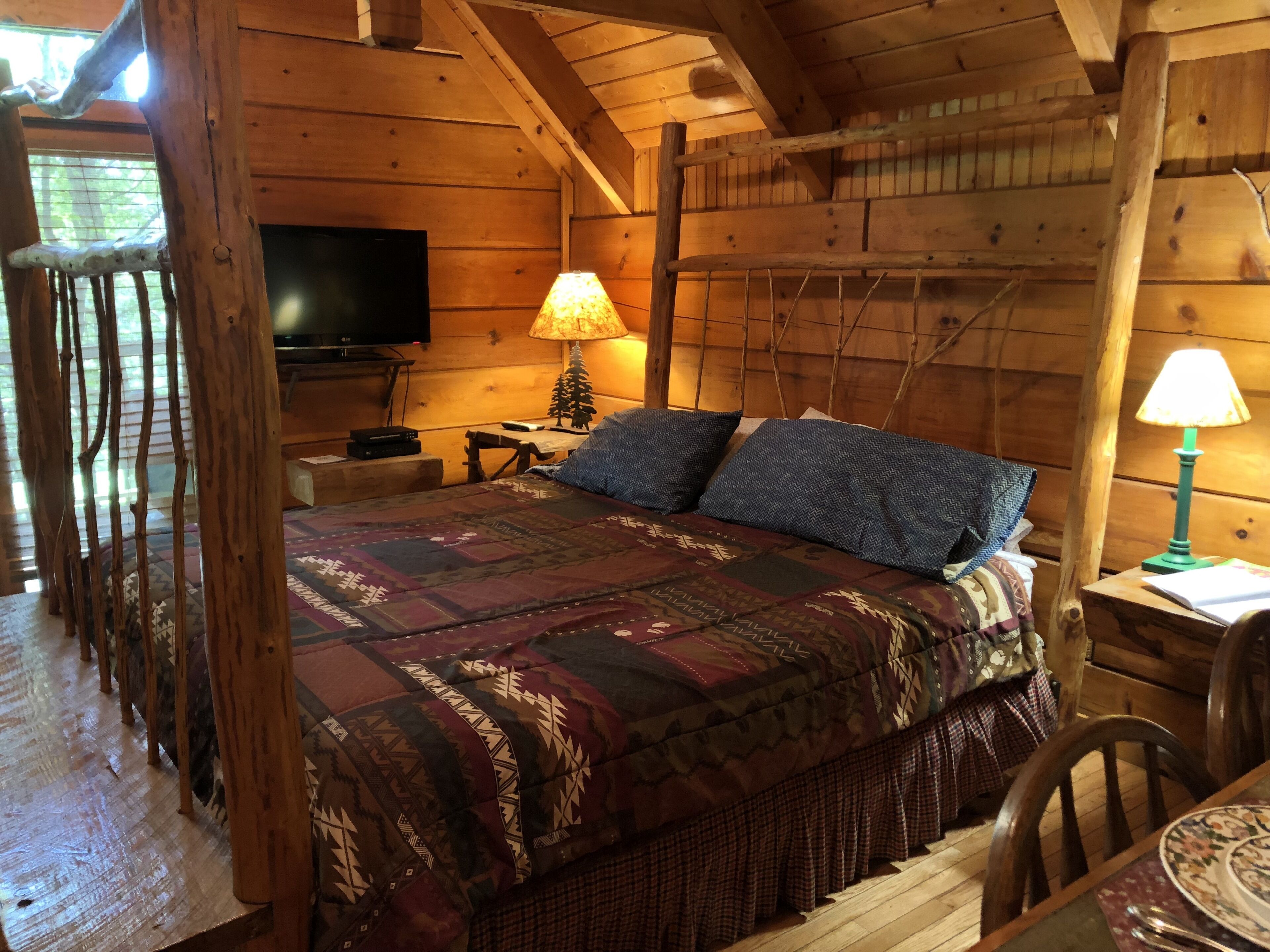 A cozy log cabin room with a bed, a television, and a lamp.