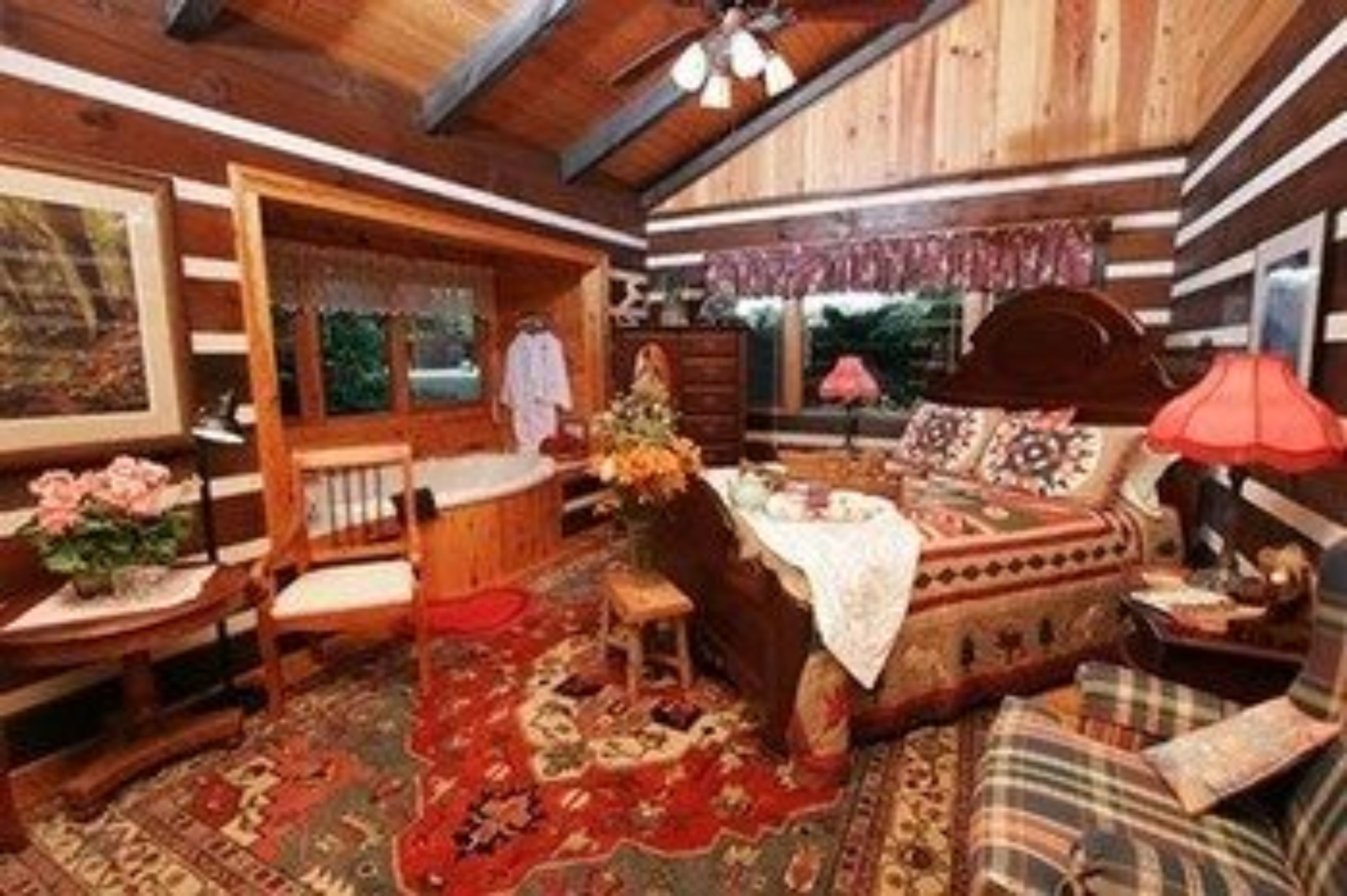 A cozy log cabin interior with a bed, wooden furniture, and a large window.