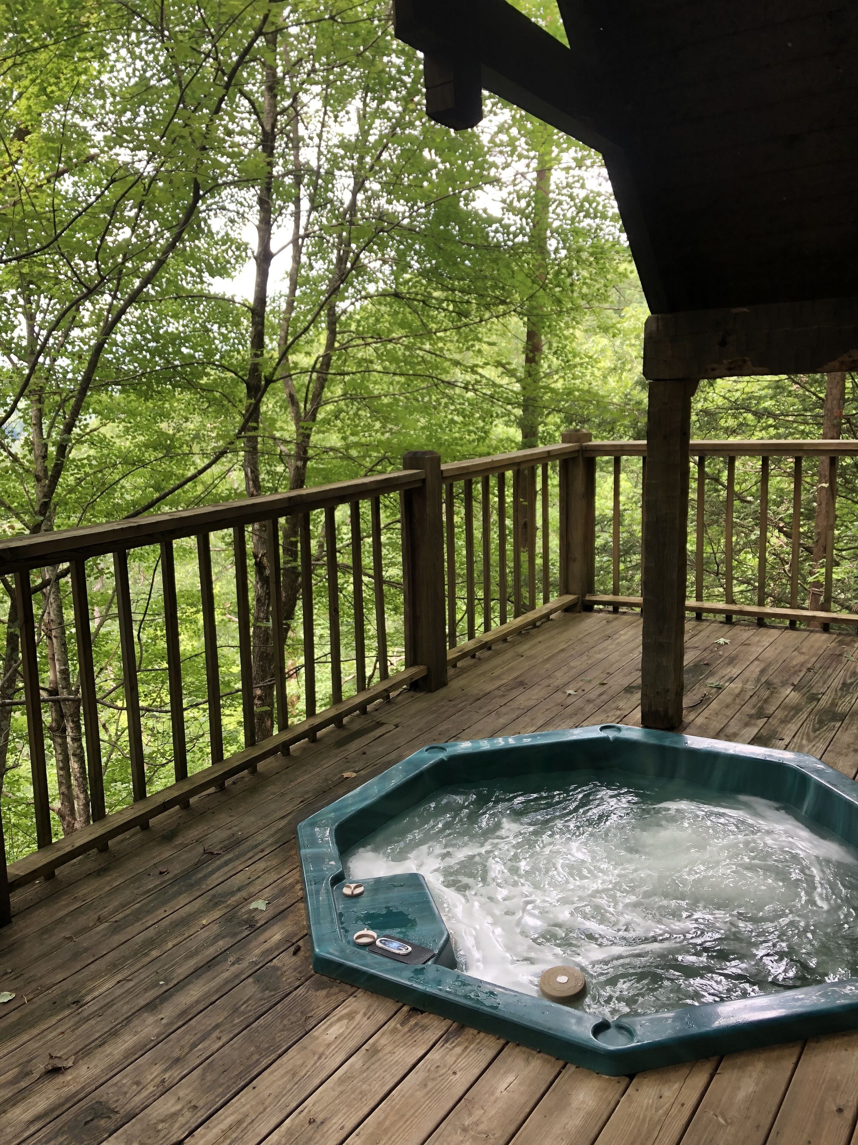 A wooden deck with a hot tub surrounded by trees.