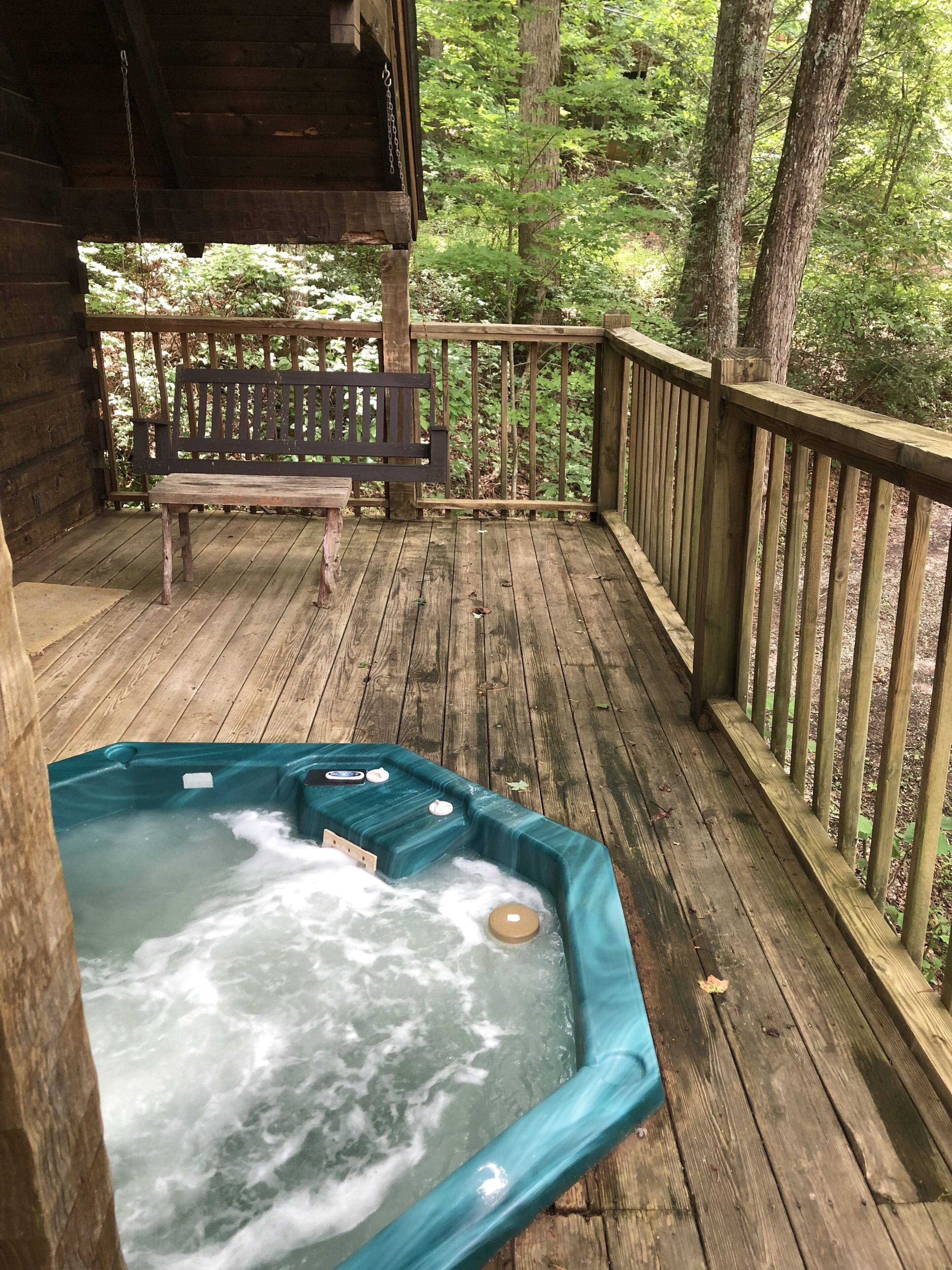 A wooden deck with a hot tub, a bench, and a wooden railing.