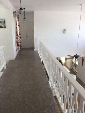 A corridor with a white railing, a door at the end, and a ceiling fan.