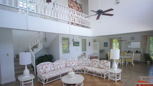 A spacious living area with a high ceiling, a white staircase, a sectional sofa, a round coffee table, and a dining area with chairs and a table. - Burlingame Villa (Montego Bay)
