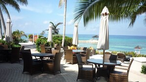 Un espace extérieur aménagé avec des meubles en osier et des parasols, offrant une vue sur une plage et l’océan.
