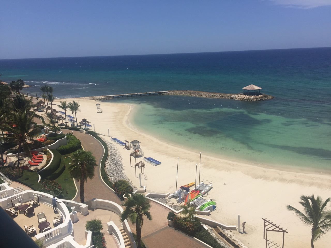 A beach resort with a curved walkway, lounge chairs, and a lifeguard tower.